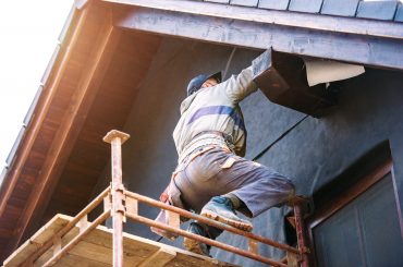 Construction worker standing on scaffold thermally insulating house facade with glass wool and black foil.