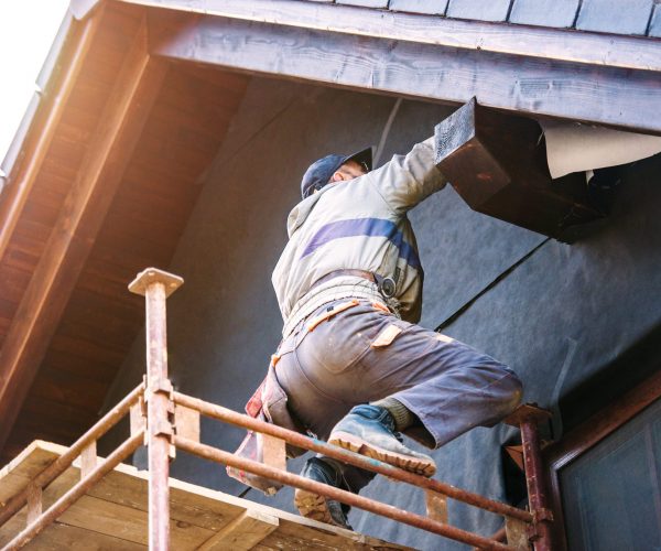Construction worker thermally insulating house with glass wool and foil. Construction worker standing on scaffold thermally insulating house facade with glass wool and black foil.
